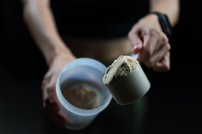 Close up of a person with measuring scoop of whey protein and shaker bottle, preparing protein shake.
