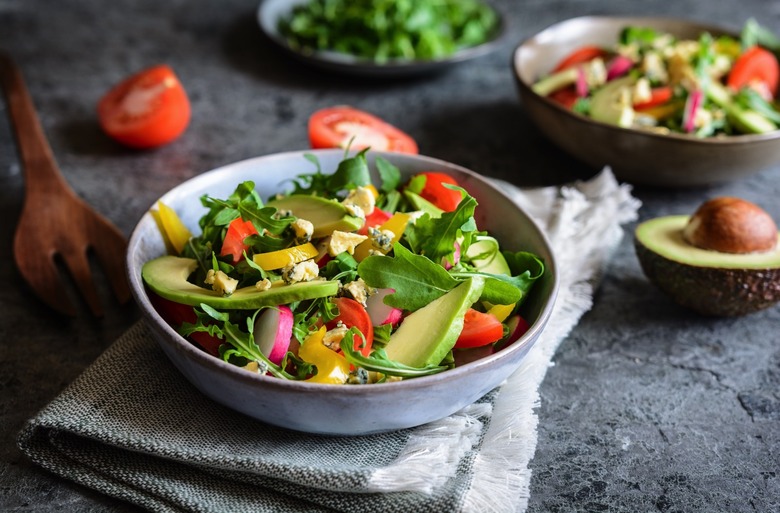 Healthy raw arugula salad with avocado, radish, bell pepper, tomato and Roquefort cheese.