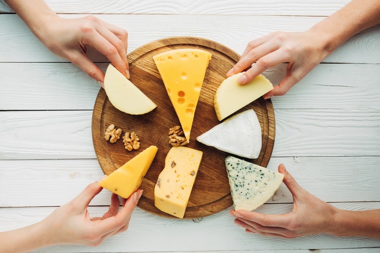 People choosing various types of cheese products from a platform.
