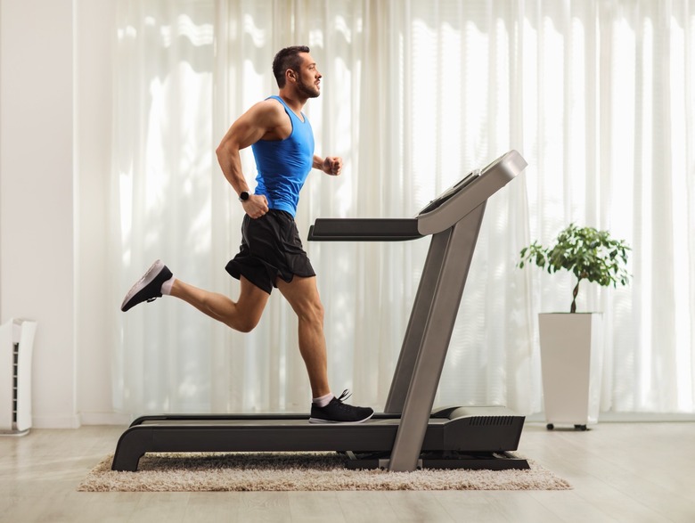 A young man running on a treadmill at home.