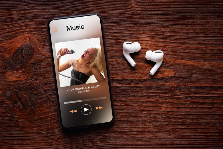 Music player on screen of iPhone and AirPods Pro on wooden surface.