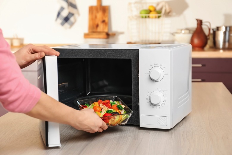 A person putting a bowl with vegetables in the microwave.