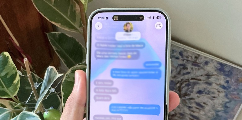 An iPhone 16 Pro Max running iOS 26 showing the new wallpaper feature on an iMessage chat