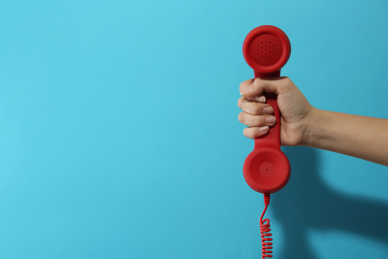 Closeup view of woman holding red corded telephone handset on li