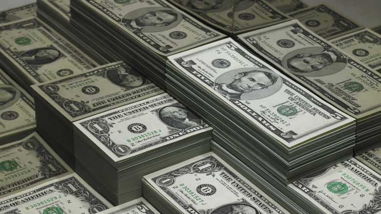 Stacks of U.S. dollar bills piled together, including bundles of one-dollar and five-dollar notes.