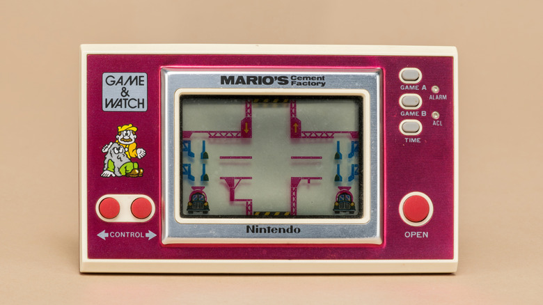 Front view of a vintage Nintendo Game & Watch handheld console displaying "Mario's Cement Factory" on a pink and white casing.