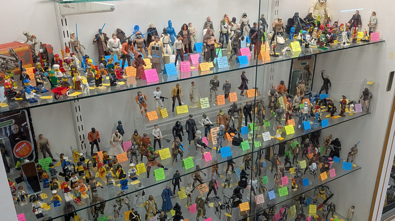 Glass display case filled with collectible action figures, LEGO minifigures, and sci-fi characters arranged on multiple shelves with colorful price tags.