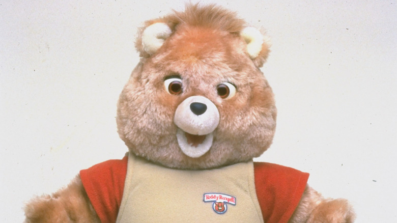 Close-up of the vintage Teddy Ruxpin animatronic teddy bear character with brown fur, wide eyes, and a tan outfit with red sleeves.