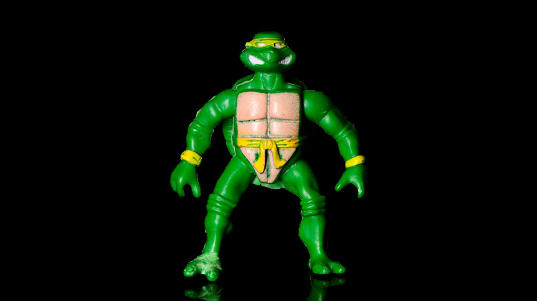 Green Teenage Mutant Ninja Turtles action figure with a yellow mask and belt standing against a black background.