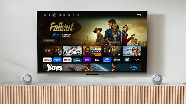 An Amazon TV on a wall in a living room with two small speakers on a cabinet below.