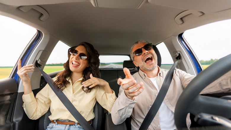 Two people singing and dancing to music while driving and riding in a car.