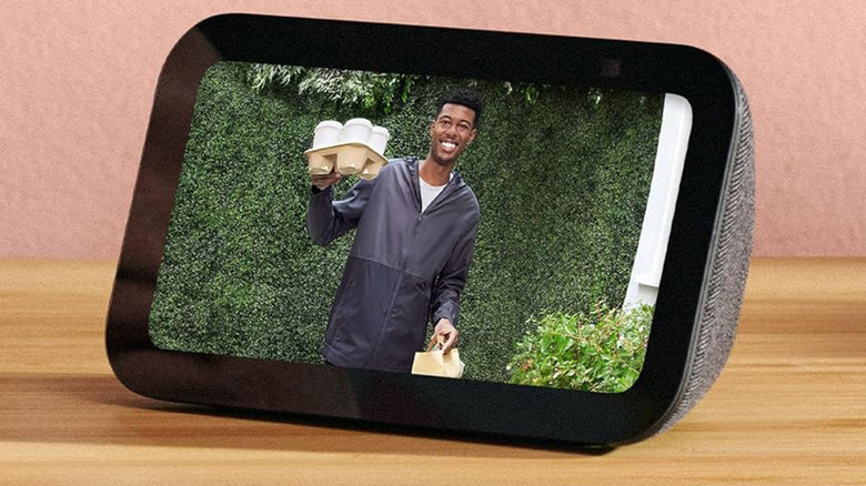 An Amazon Echo Show 5 on a wooden table against a pink background.