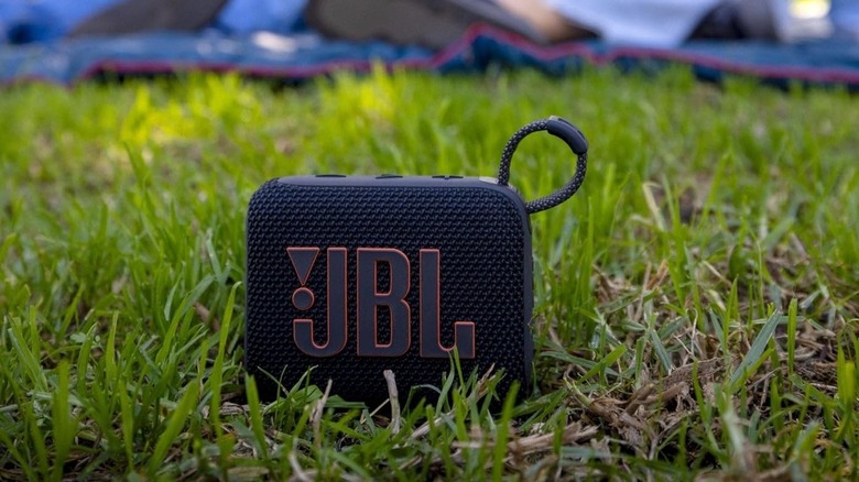 The JBL Go 4 Bluetooth speaker outdoors, placed on the ground with grass.