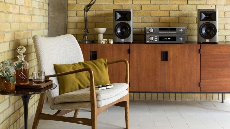 A high-end home audio listening room featuring bookshelf speakers, stereo amplifier components, and mid-century modern furniture arranged against an exposed brick wall.
