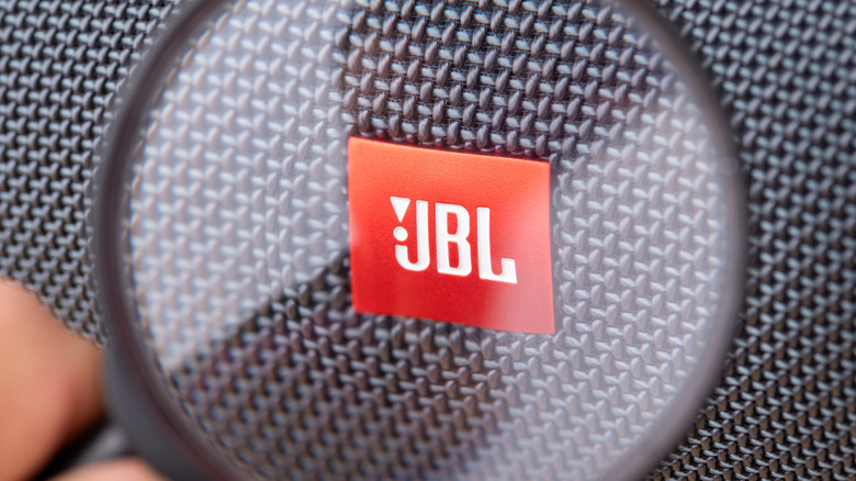 Close-up magnified shot of a JBL speaker grille, highlighting the red JBL logo badge against the textured woven fabric surface.