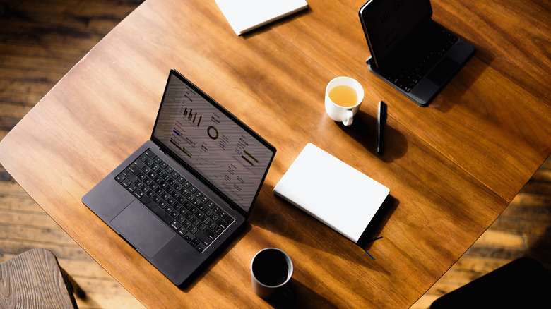 Wooden table with a laptop, notebook, notepad, tea cup, and coffee cup