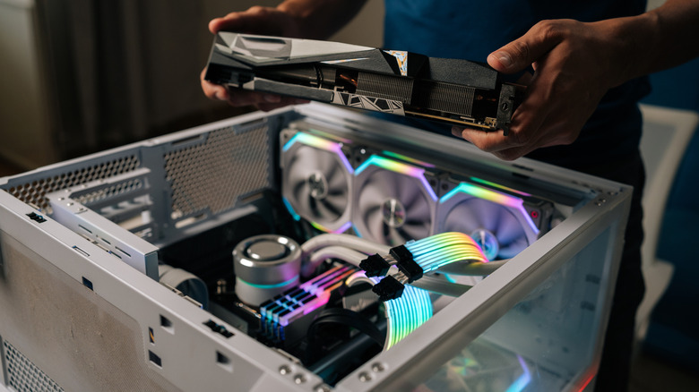 A man holding a PC component above an open PC case with RGB lighting