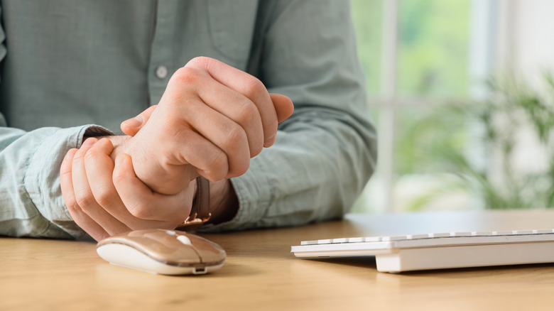 A person holding his wrist near a wireless mouse on a desk.