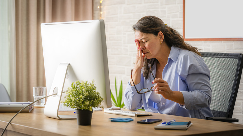 A woman touching her strained eyes while in front of a monitor.