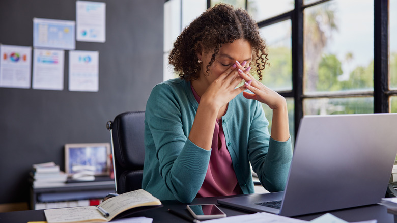 A woman looking exhausted in front of a laptop in a home office.