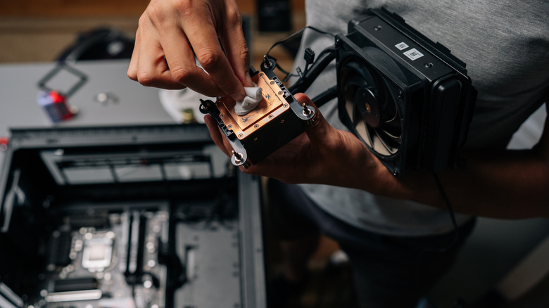 A person cleaning the CPU heat sink with the fan held near it