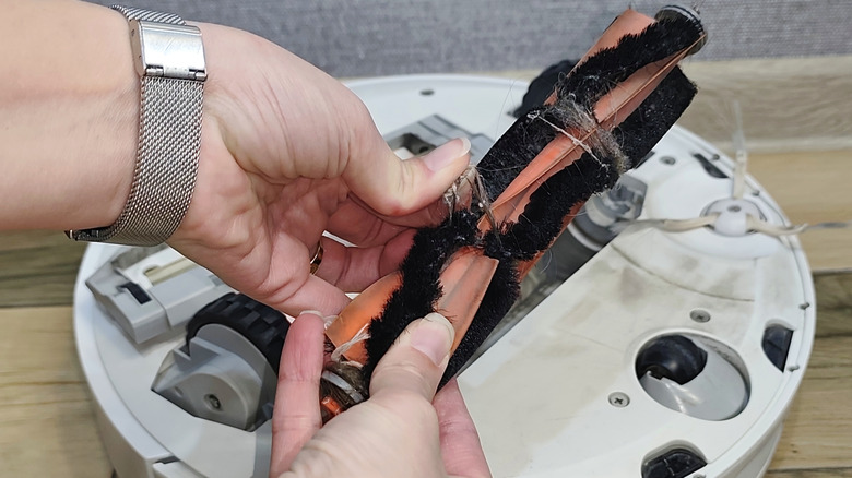 A close-up of hands removing a dirty brush roller from a white robot vacuum