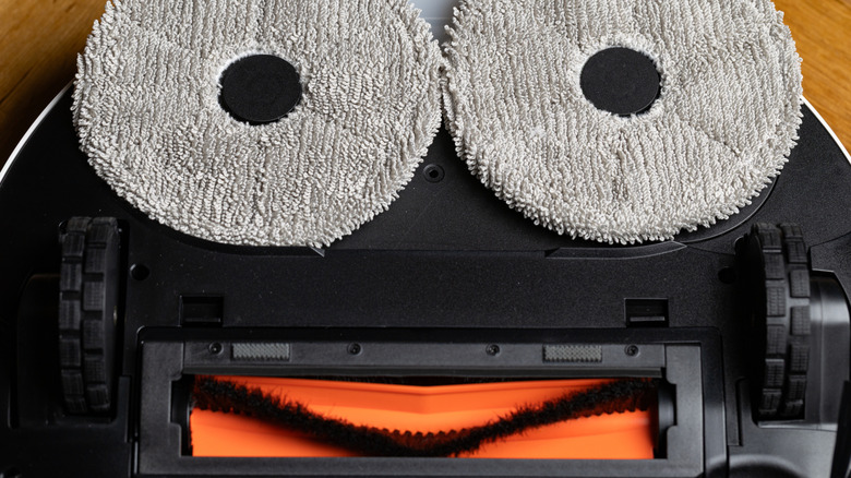 The black underside of a robot vacuum showing a vacuum roller and two gray mop pads