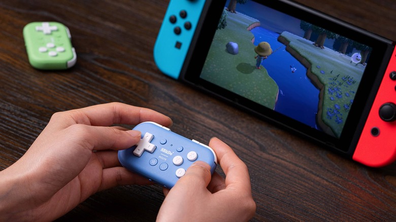 A person holding the 8Bitdo Micro controller in their hand, playing Animal Crossing on a Nintendo Switch. Another green 8Bitdo Micro sits in the background.
