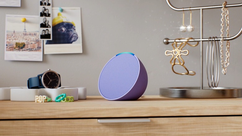 The Amazon Echo Popsmart speaker placed on a table, surrounded by a watch, a decorative stand, and other desk decorations