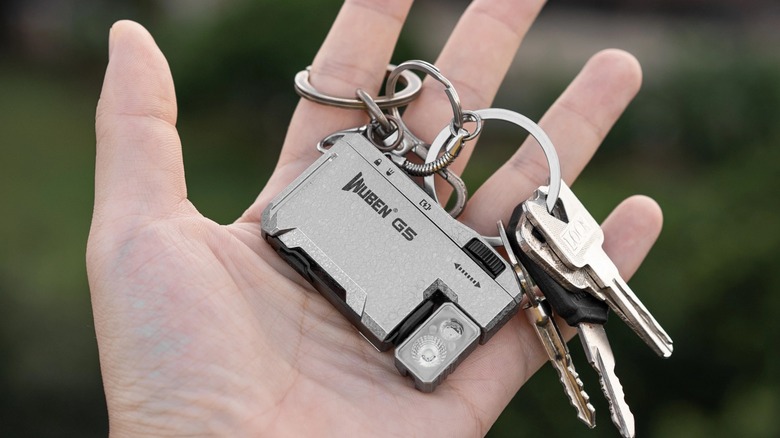 A hand holding the Wuben G5 flashlight attached to a keychain.