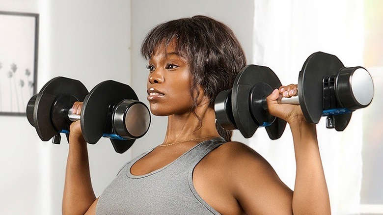 A woman lifting the LifePro PowerFlow Plus Adjustable Dumbbells as part of her workout.