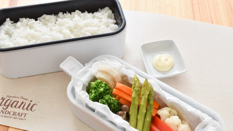 The Bento rice cooker on a desk with rice and vegetables in the two chambers