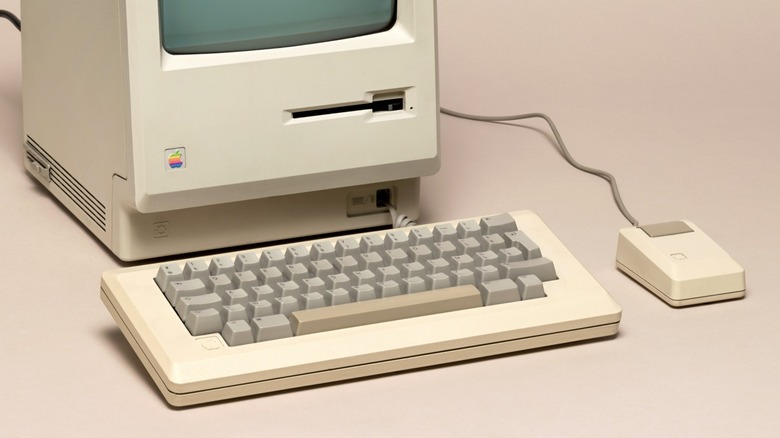 A retro keyboard in front of an Apple Macintosh computer