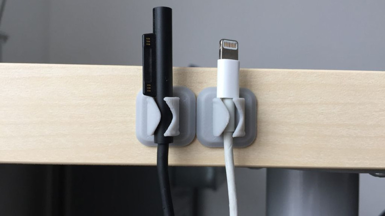 Two 3D printed cable holders on the side of a desk, holding cables.