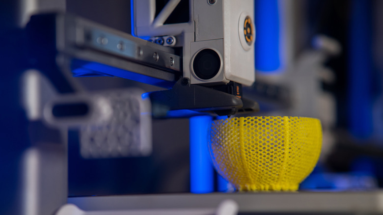A close up of a 3D printer in the middle of printing a yellow object.