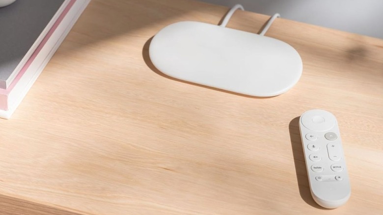 The Google TV Streamer 4K with its remote on a wooden TV console table.