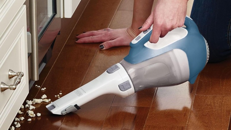 A person using the Black+Decker Dustbuster CHV1410L handheld vacuum to pick up popcorn on the floor.
