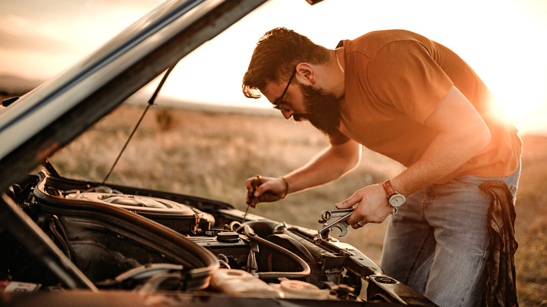 A man looking into car engine compartment with its hood open.