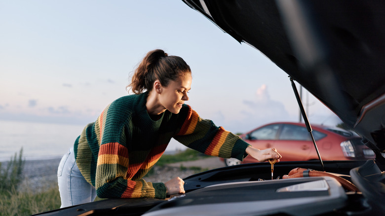 A woman checking the dipstick of a car.