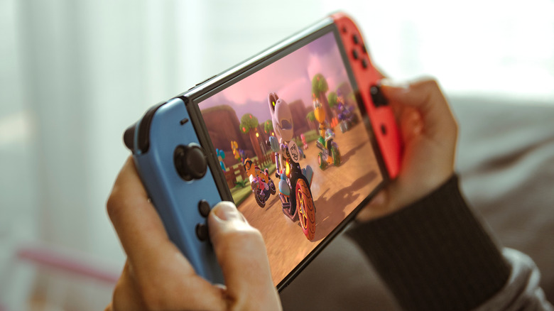 Close-up of a person holding a Nintendo Switch console with red and blue Joy-Cons while gaming indoors.