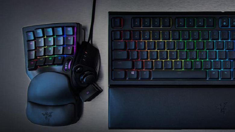 An RGB-lit Razer Tartarus V2 gaming keypad and wrist rest on a dark desk beside a backlit keyboard.
