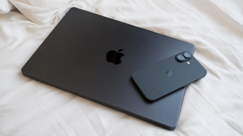 An iPhone on top of a closed MacBook against a white cloth background.