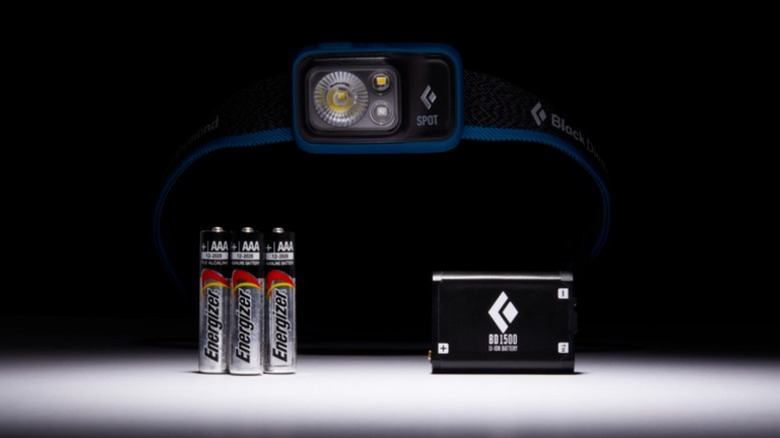 A front of the Black Diamond Spot 400 headlamp, three AAA energizer batteries, and the Black Diamond rechargable battery pack.