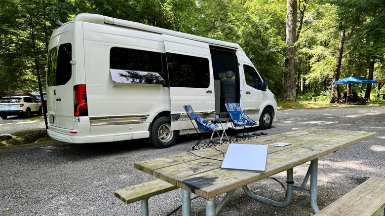 The Starlink Mini satellite antenna sitting on top a table. A camper win is parked right behind with camping chairs in front.