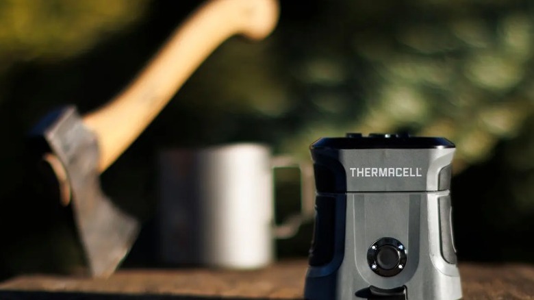 Thermacell E-Zone Guard Adventure mosquitor repellant system sitting on a chopping block. An axe and a mug are in the background.