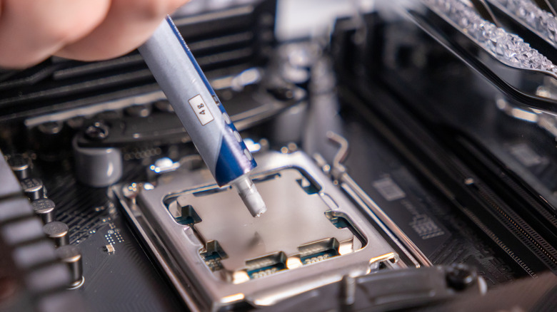 A close-up of a person applying thermal paste on top of a desktop CPU.