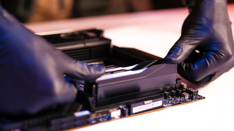 A close-up of a person installing RAM sticks into a desktop motherboard.