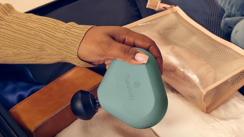 The TheraGun being pulled out a pile of luggage held in someone's hand