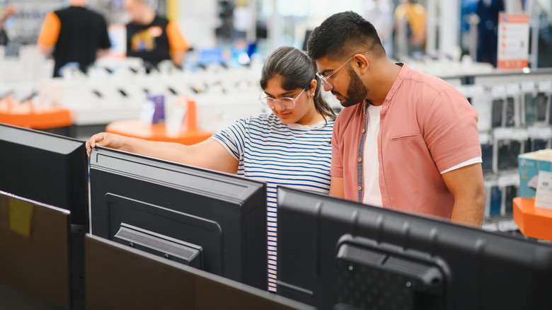 A couple inspects TVs on display in a store.