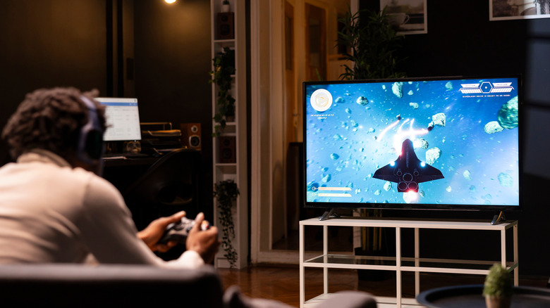 A person wearing headphones plays a video game on a TV.